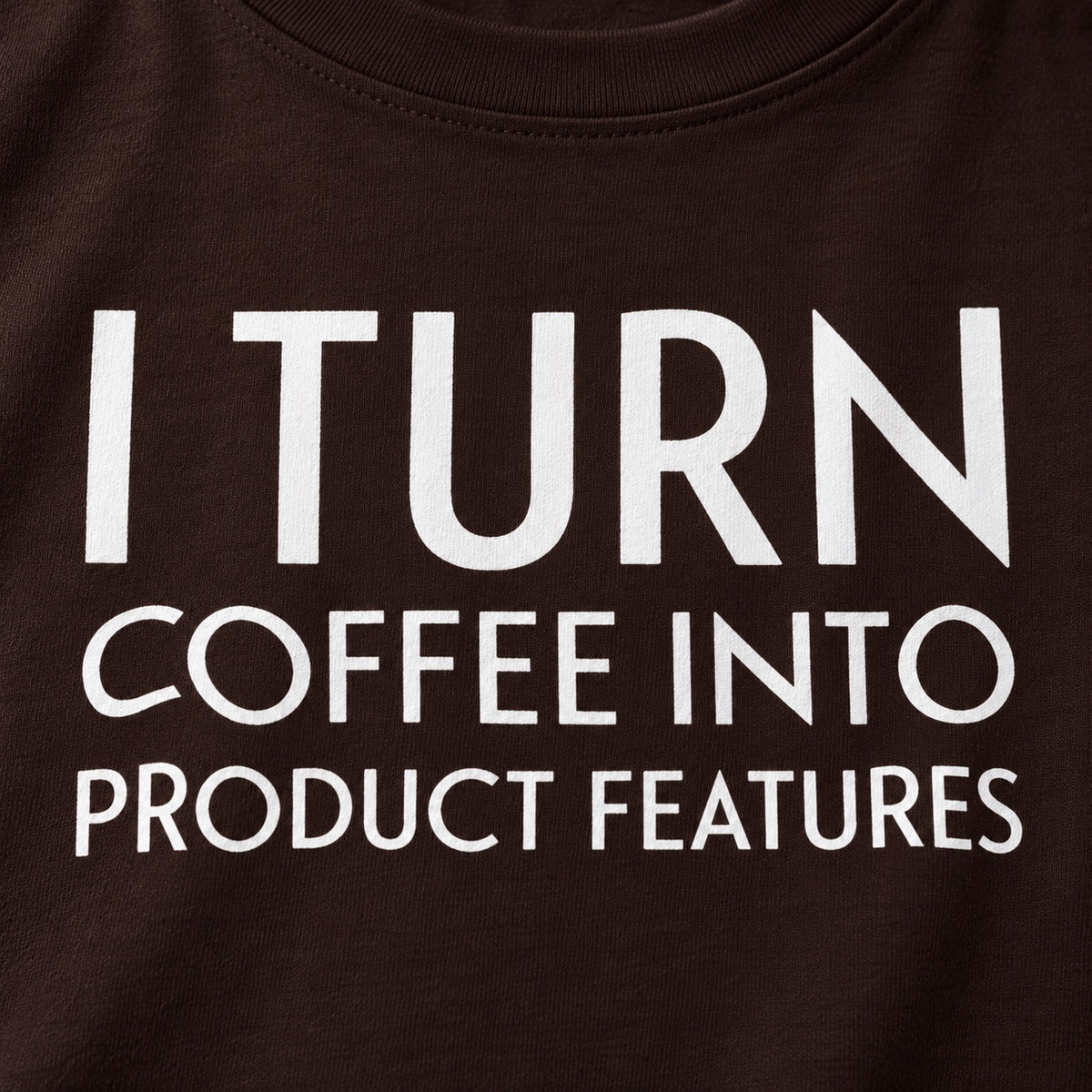 Close-up of the white I Turn Coffee Into Product Features print on brown cotton
