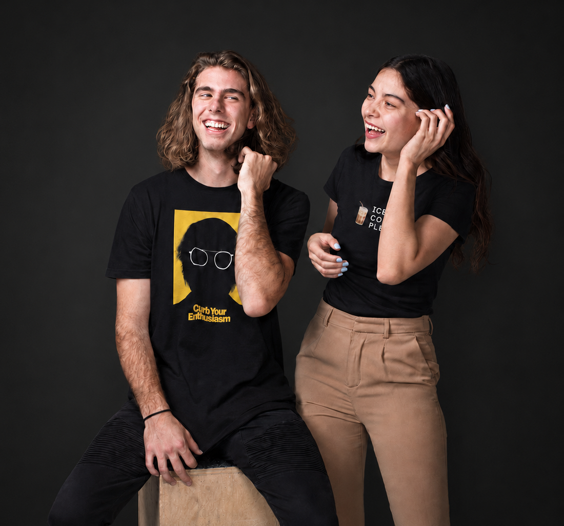 Two friends laughing in black printed tees on a dark studio backdrop